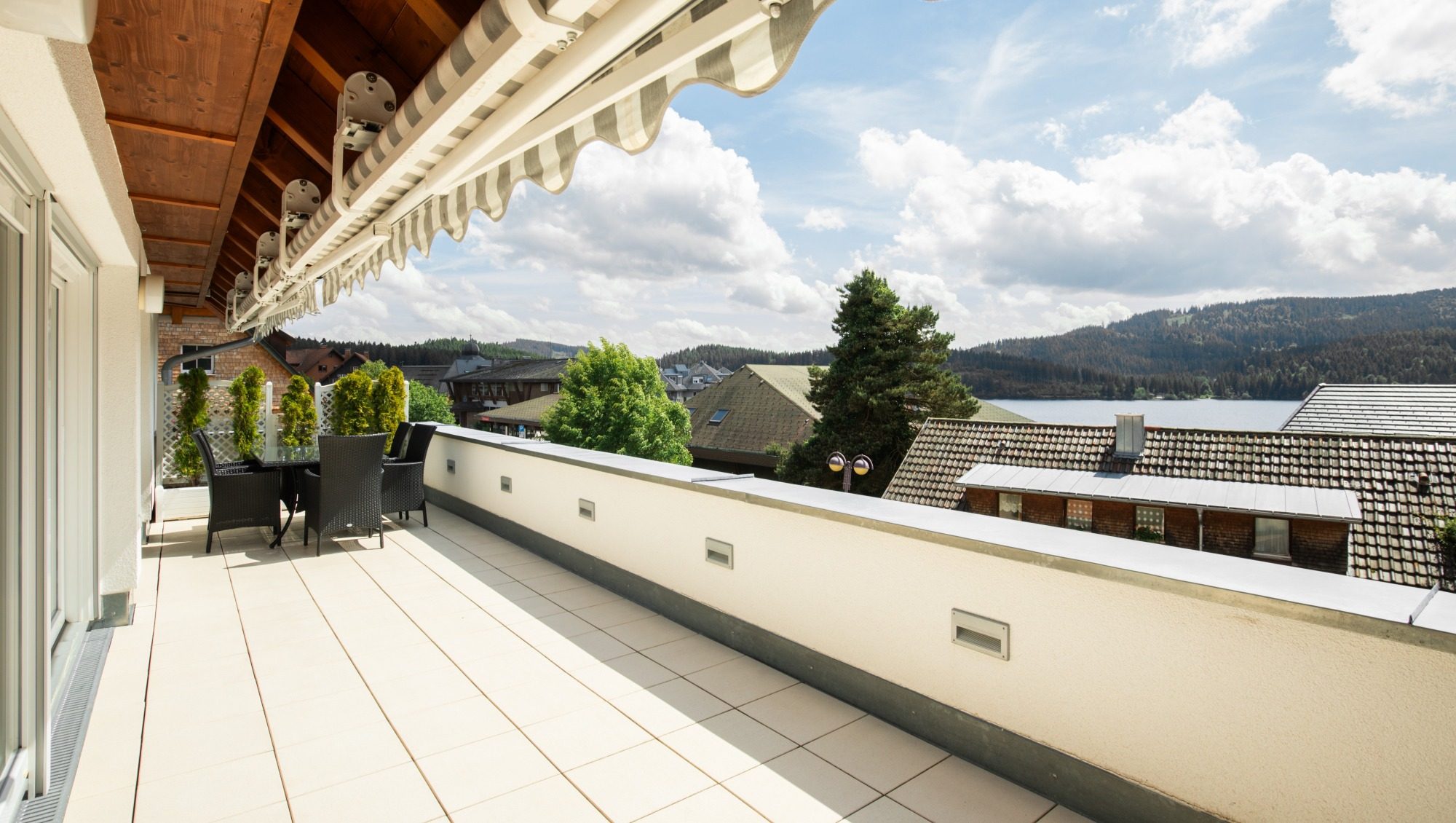 Terrasse mit Blick auf den Schluchsee, davor Hausdächer, im Hintergrund der Terrasse ist eine Sitzgruppe angeordnet.
