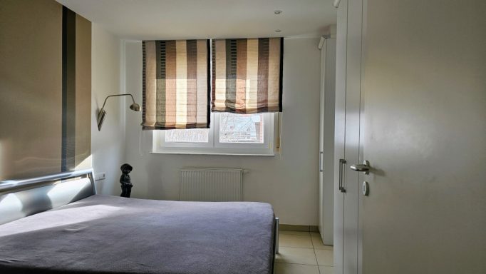 Helles Schlafzimmer mit einem Bett, einem Fenster und gestreiften Vorhängen.