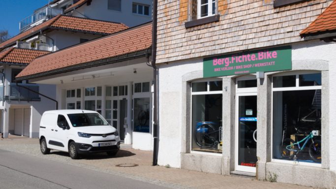 Weißes Lieferfahrzeug vor einem Geschäft mit Fahrrädern in der Auslage.