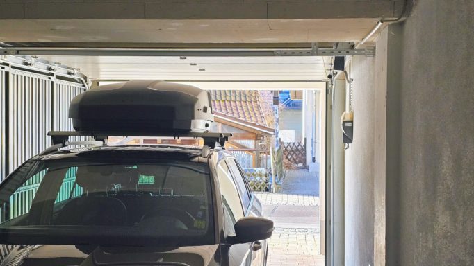 Ein Auto mit Dachbox steht in einer Garage mit geöffnetem Tor.
