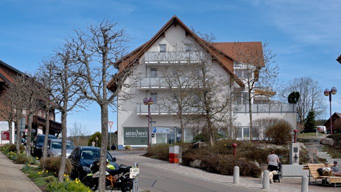 Mehrstöckiges Gebäude mit modernem Design, umgeben von Bäumen und Parkplätzen.