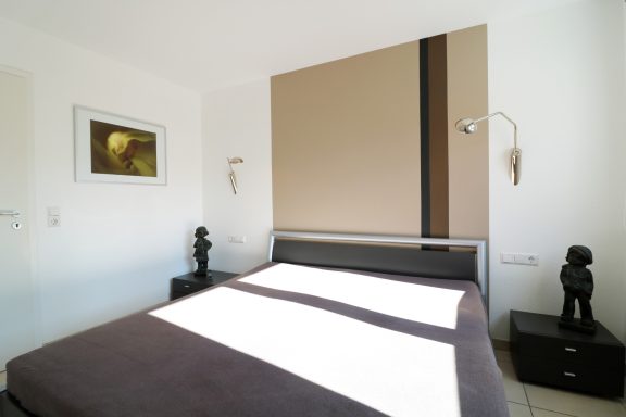 Schlafzimmer mit einem Bett, Nachttischen und modernen Wandlampen.