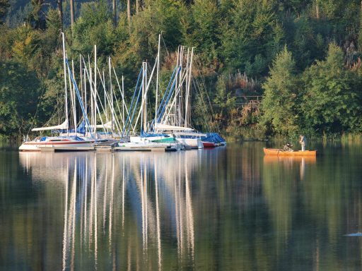 Zahlreiche Yachten und ein Kanu spiegeln sich in einem ruhigen Gewässer.