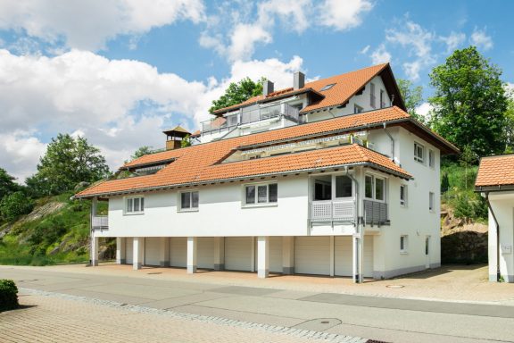 Weißes Gebäude mit rotem Dach, umgeben von Bäumen und einem blauen Himmel.