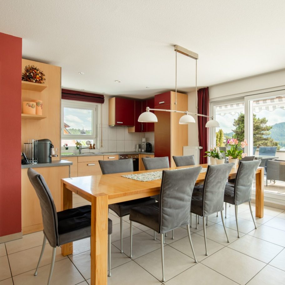 Offene Küche mit Essgruppe, acht Stühlen, im hinteren Bereich Küchenschränke, auf der rechten Seite Glasschiebeelemente zur Terrasse.