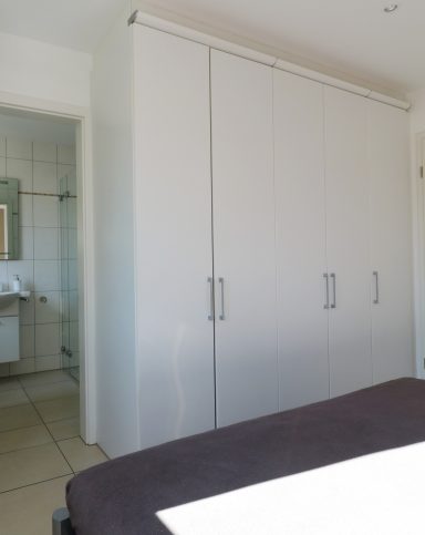 Weißer Kleiderschrank in einem hellen Raum mit Blick auf ein Badezimmer.