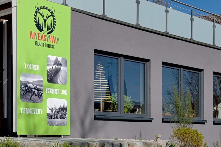 Graue Fassade mit drei großen Fenstern von MY EASY WAY mit grüner Werbetafel und der Aufschrift Touren Vermietung Teamevents.