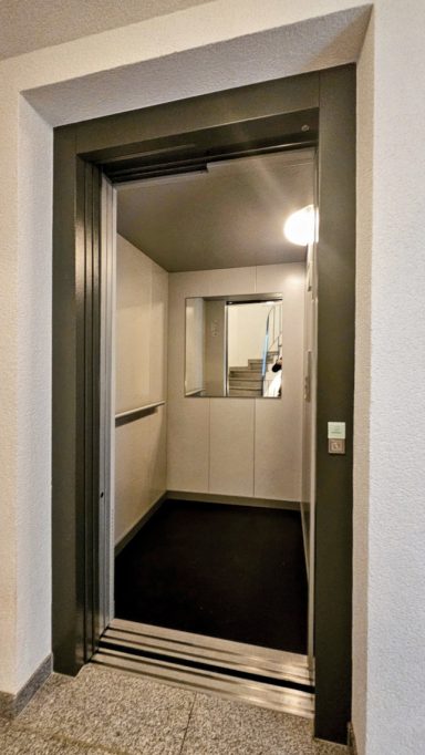 Modern Aufzug mit offener Tür, speziellem Bodenbelag und Spiegel im Inneren.